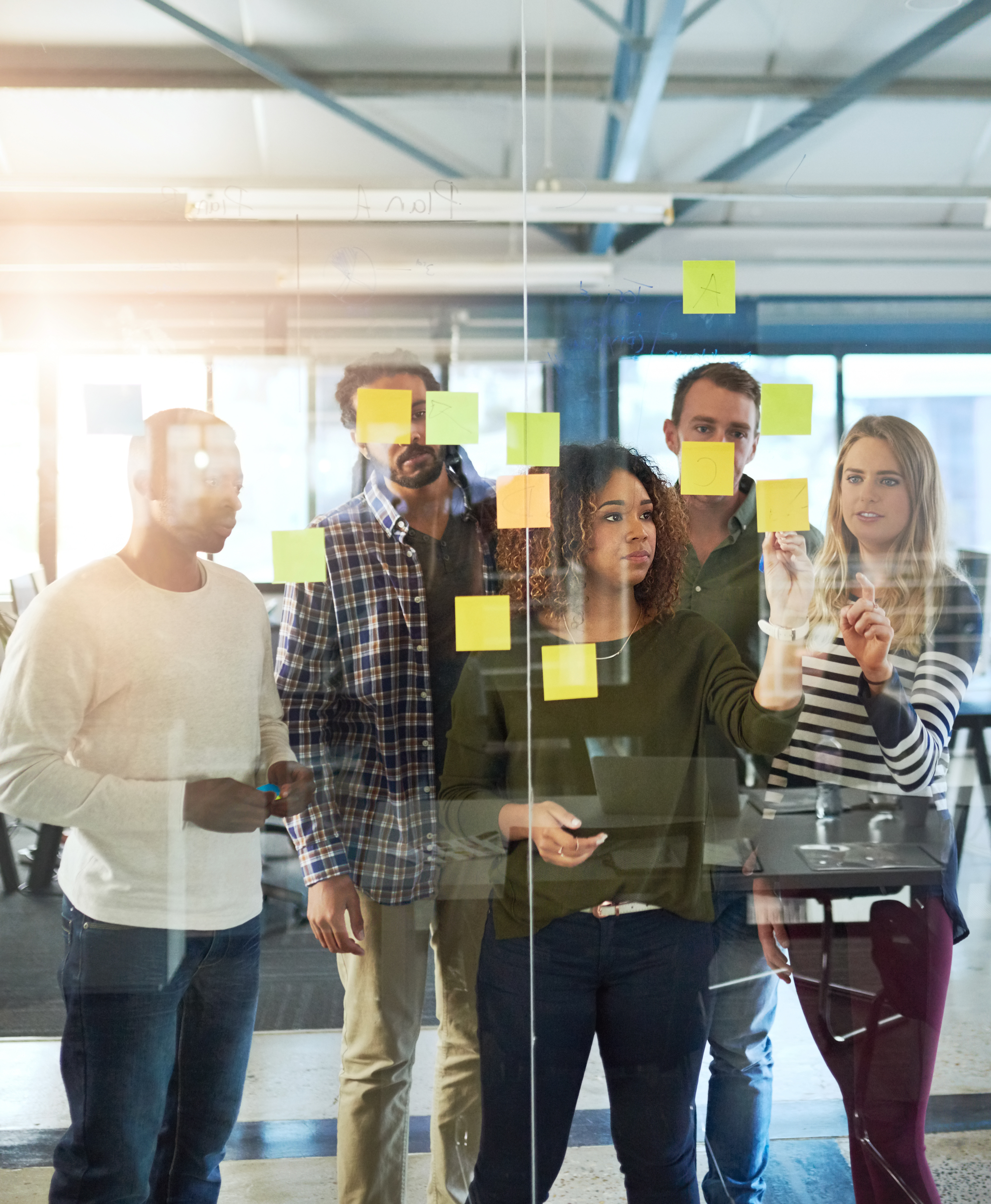 A group of students arrange post-it notes on a glass wall.