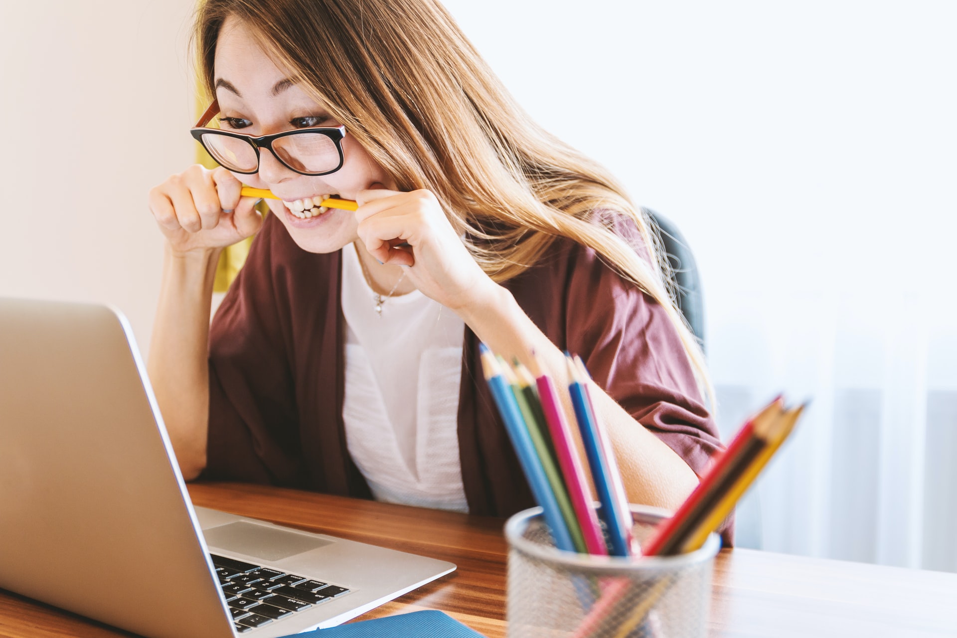 A woman sitting at a table using a computer while biting a yellow pencil